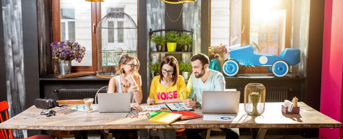 Group of caucasian coworkers dressed casually working together with documents and laptops at the big table in the beautiful cafe interior